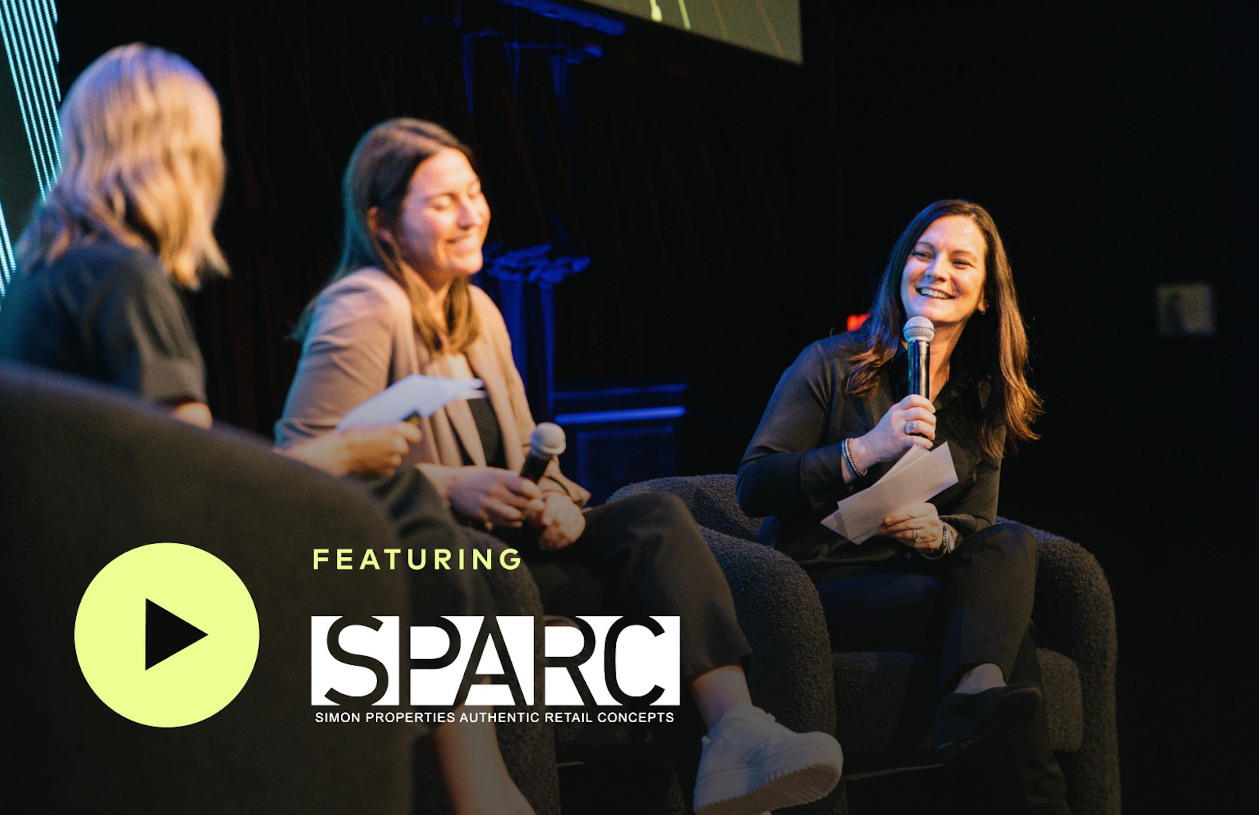 Three women smiling and sitting onstage at Amplify. Featuring SPARC Group.