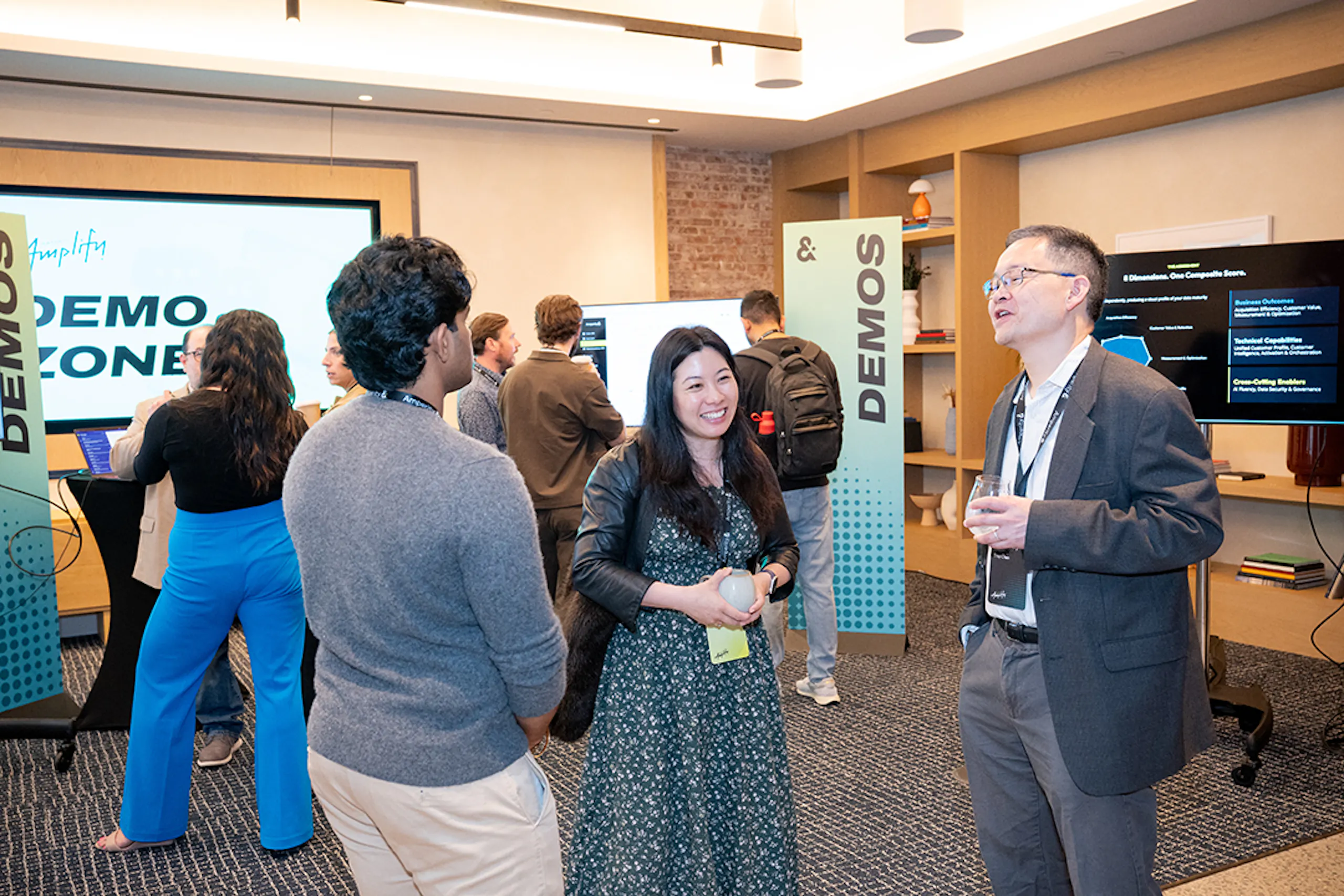 A smiling woman and two men mingling in the Demo Zone at Amplify 2026.