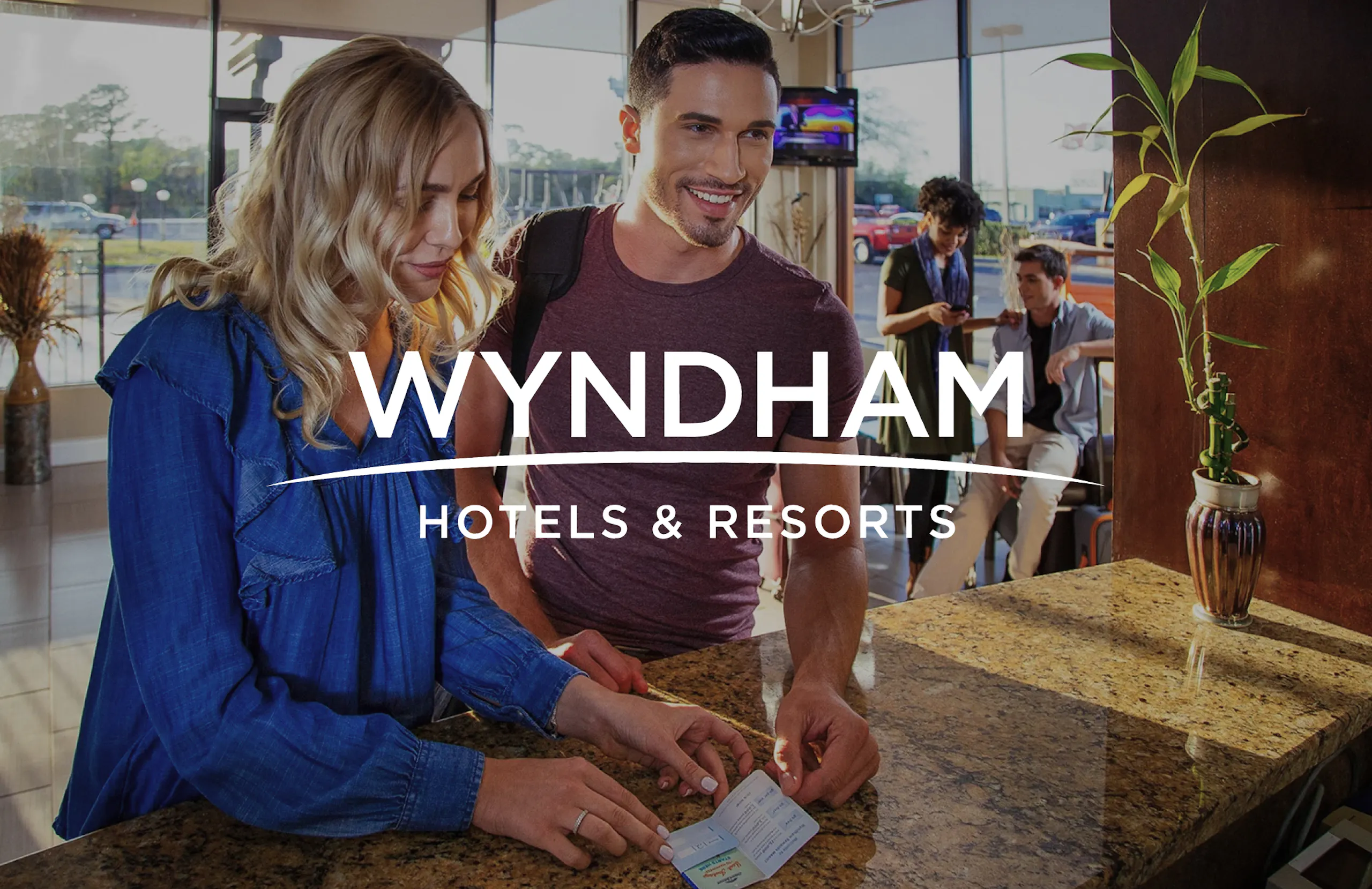 Wyndham Hotels logo overlaid on a photograph two people checking in at one of their properties