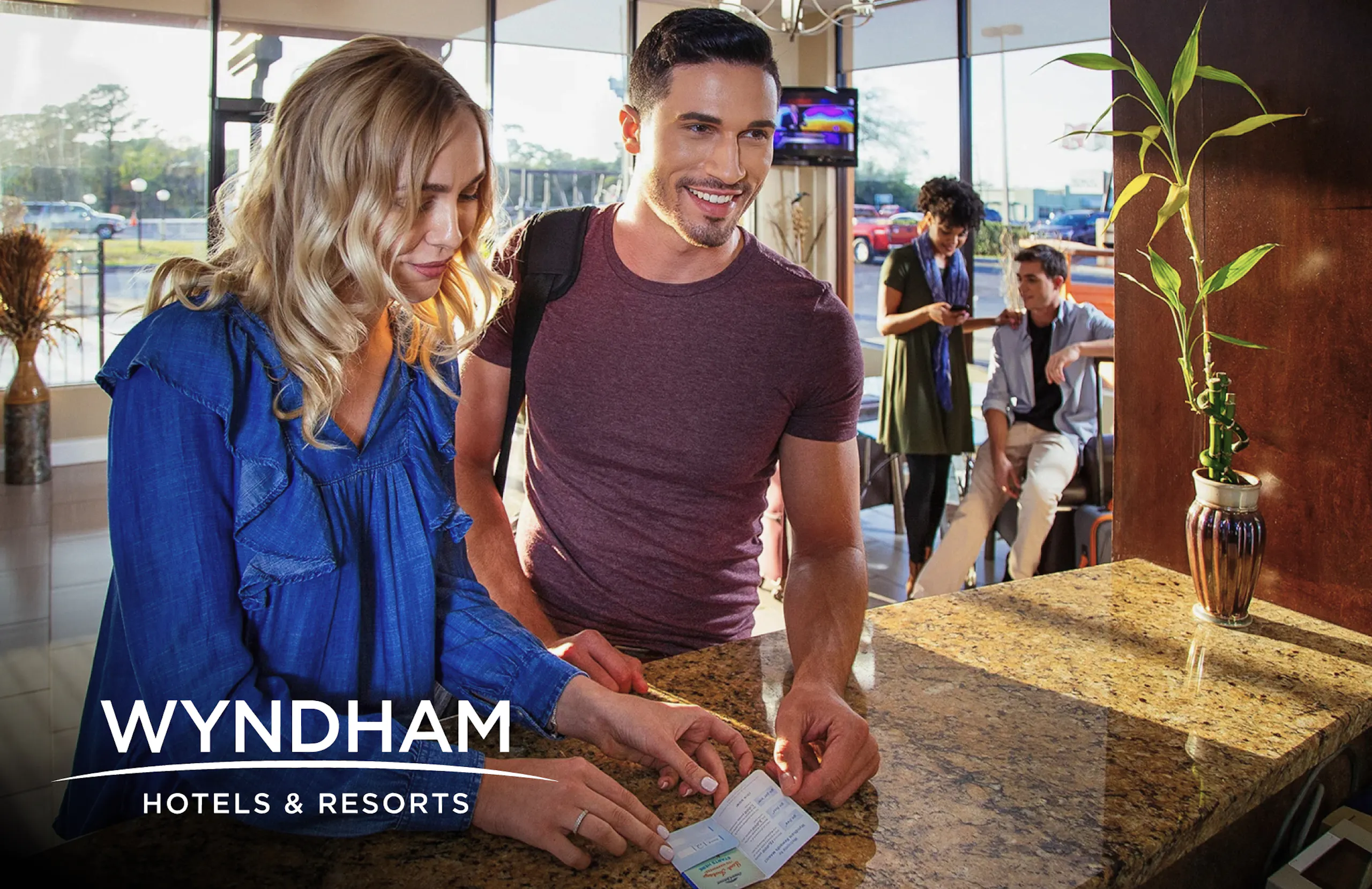 Wyndham Hotels logo overlaid on a photograph two people checking in at one of their properties