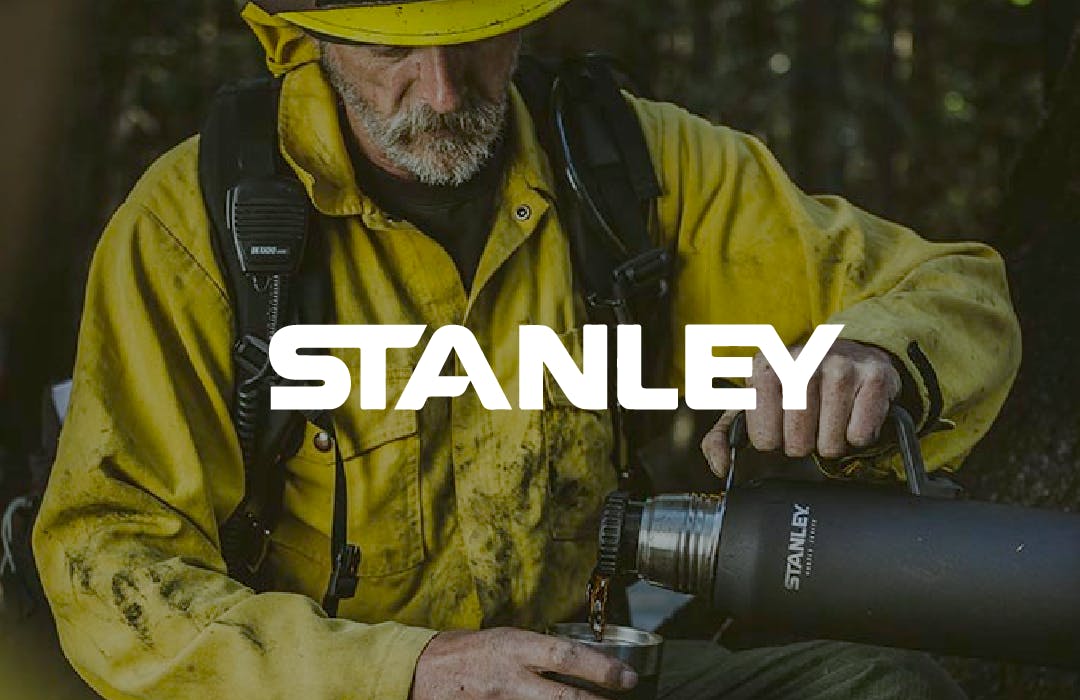 Man in stained yellow coveralls and helmet, pouring a drink out of a Stanley thermos, overlaid with the Stanley logo.
